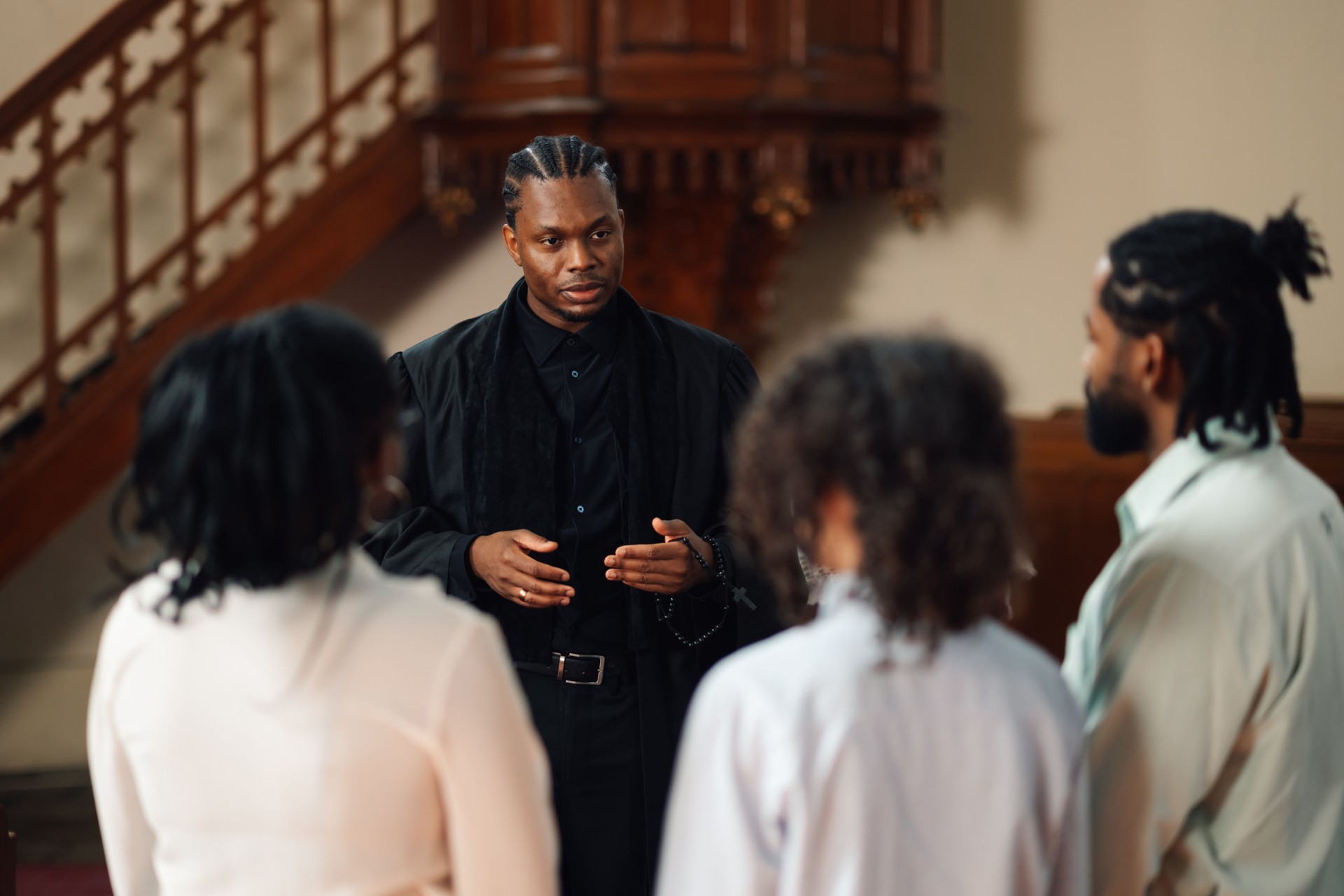 Young priest holding rosary beads talking to group in church